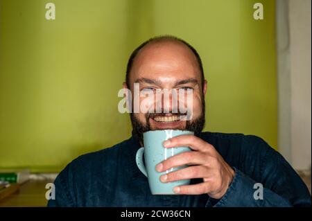 Mann mit Kaffeetasse in der Hand lacht freundlich an der Kamera Stockfoto