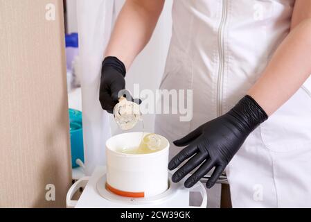 Wachserhitzer mit heißem gelbem Wachs auf Holzspatel in menschlicher Hand. Heißes Wachs für Enthaarung. Salonausstattung Stockfoto