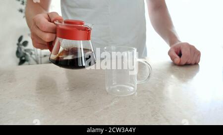 Der Mann gießt einen frisch gebrühten Kaffee in eine Glastasse vom Glasserver. Pourover, V60. Stockfoto