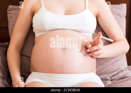 Schwangere Frau Rauchen Zigarette zu Hause im Bett. Stockfoto