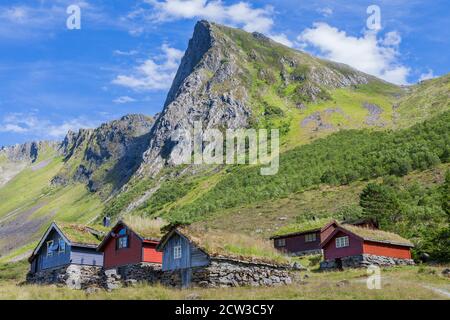 ROMEDALEN, NORWEGEN - 2014. JULI 21. Alte traditionelle Bauernhäuser mit Gras auf dem Dach in der Mitte des Tales mit großem Berg dahinter. Stockfoto