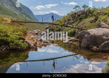 ROMEDALEN, NORWEGEN - 2014. JULI 21. Ein Kind steht auf einer Brücke über den Fluss mit einer Spiegelung der Szene im Vordergrund. Stockfoto