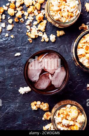 Eis Cola und Karamell Popcorn, ungesunde Speisen und Getränke, schwarzer Tisch, Draufsicht Stockfoto