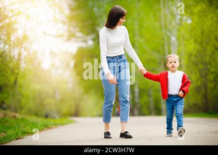 Glückliche kaukasische Familie Mutter und Sohn Kind gehen im Park Hände, Sonnenlicht halten Stockfoto