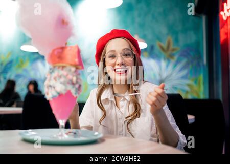 Süßes Dessert mit rosafarbener Baumwollbonbons, Milchshake und Kuchen. Mädchen in rotem Beret und Brille, Café in Frankreich Stockfoto