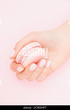 Mädchen hält Hände Macaron Cookies. Stilvolle trendige weibliche Maniküre auf rosa Hintergrund Stockfoto