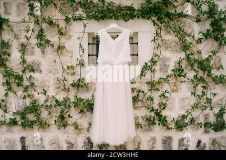 Eine Wand aus Stein mit verdrehten Jasminzweigen mit einem Fenster und einem Hochzeitskleid in der Mitte verschlungen. Stockfoto