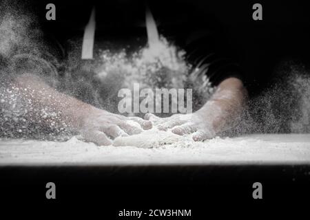 Die Hände der männlichen Bäcker Zubereitung Hefeteig mit weißem Mehl Staub auf schwarzen Hintergrund, Schaufel für Pasta und Pizza Stockfoto