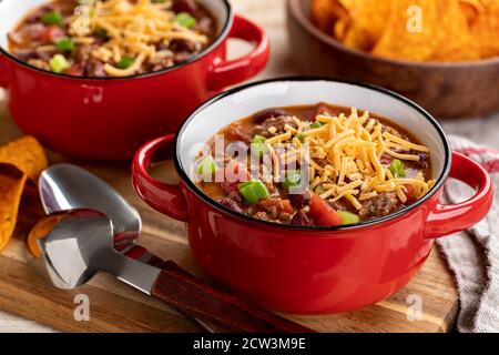 Schüssel Chili con Carne mit geschreddertem Cheddar-Käse auf Ein Holzbrett Stockfoto