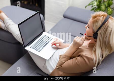 Fokussierte aufmerksame Frau in Kopfhörer sitzt mit Laptop, schaut auf den Bildschirm, macht Notizen, lernt Fremdsprache im Internet, Online-Studium, selbst Stockfoto