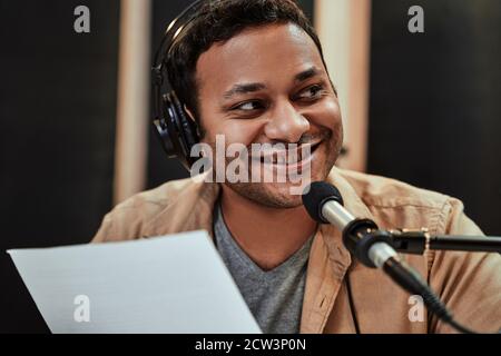 Nahaufnahme Porträt von glücklichen jungen männlichen Radio-Host in Kopfhörer lächelnd neben, während sprechen, Rundfunk im Studio Stockfoto