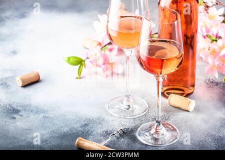 Rosé Weinglas mit Flasche auf dem grauen Tisch und rosa Blumen. Rosado, rosato oder Rouge Weinprobe im Weinshop, Bar-Konzept. Speicherplatz Kopieren Stockfoto