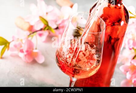 Roséwein aus der Flasche, grauer Background, rosa Blüten. Rosado, rosato oder Rouge Weinprobe im Weinshop, Bar-Konzept. Speicherplatz Kopieren Stockfoto