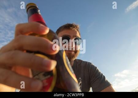 Ein junger Mann, mit Gläsern, Toast mit Bier, genießt den Sonnenuntergang in Galicien, Nordspanien. Stockfoto