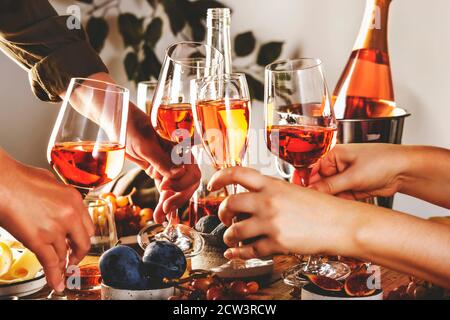 Hände halten Gläser mit Roséwein über dem Tisch serviert Für festliche Dinner-Party mit verschiedenen Arten von Vorspeisen und Früchte Stockfoto
