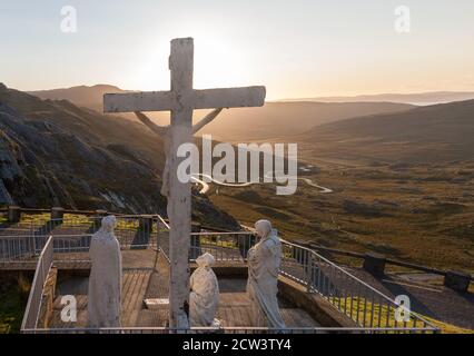 Healy Pass, Cork, Irland. September 2020. Am frühen Morgen beginnt das Sonnenlicht, die Statue der Kreuzigung auf dem Gipfel des Caha-Gebirges am Healy Pass in West Cork, Irland, zu illustrieren. - Credit; David Creedon / Alamy Live News Stockfoto