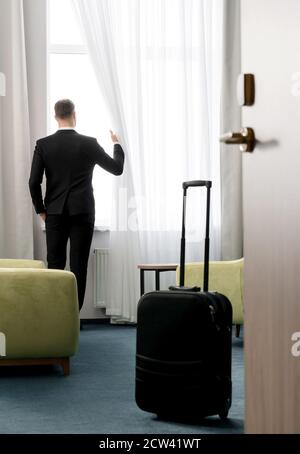 Rückansicht des Geschäftsmannes in dunklen Anzugkleidung im Hotel Zimmer mit Blick auf das Fenster Stockfoto