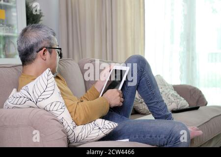 Der asiatische Mann, der sich im Wohnzimmer entspannt. Stockfoto