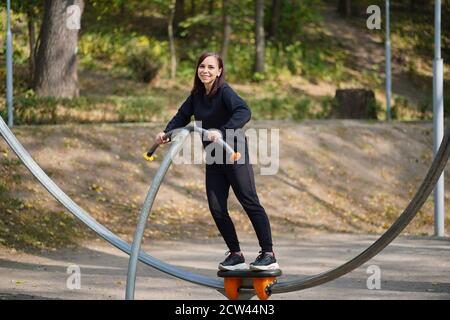 Junge Frau in Freizeitkleidung Sport im Park. Erwachsene weibliche tun Sport-Übungen auf Straße Simulator im Herbst Saison Stockfoto