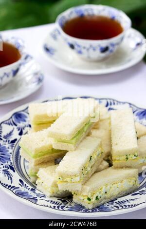 Nachmittagstee im Garten, Fingersandwiches mit Gurken und Eiersalat und Tee auf hellem Hintergrund. Stockfoto