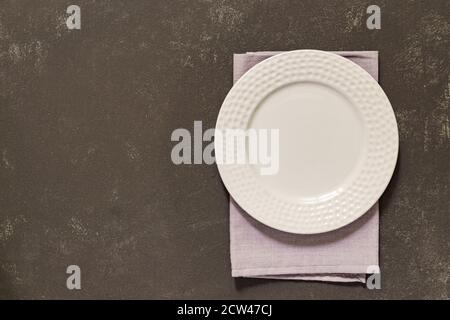 Draufsicht auf leeren geservierten Teller, graue Textilserviette auf schwarzem Beton-Hintergrund. Speicherplatz kopieren. Stockfoto