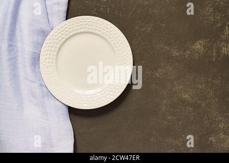 Draufsicht auf leeren gedienten Teller, blauer Stoff auf schwarzem Betonhintergrund. Speicherplatz kopieren. Stockfoto