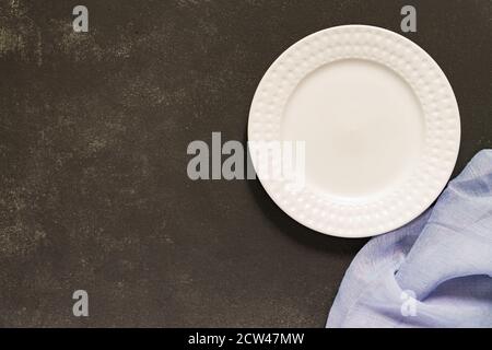 Draufsicht auf leeren geservierten Teller, graue Textilserviette auf schwarzem Beton-Hintergrund. Speicherplatz kopieren. Stockfoto