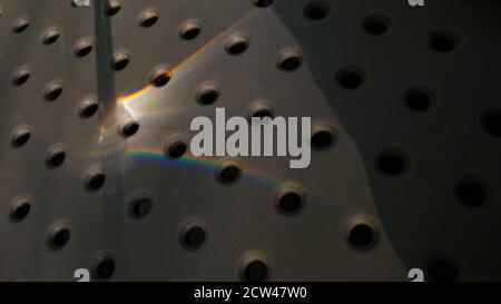 Sonneneinstrahlung des Regenbogenspektrums Licht auf gepunktete Oberfläche mit abstrakten Schatten. Kreisförmige Lochmuster Hintergrund Stockfoto