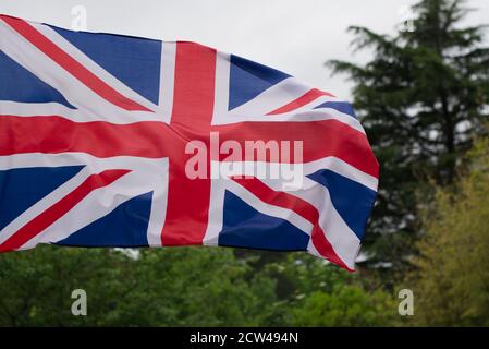 Flagge von England / Großbritannien (UK) winkt im Wind. Hintergrund mit Bäumen und Himmel nicht im Fokus. Stockfoto
