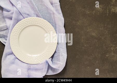 Draufsicht auf leeren gedienten Teller, grauer Stoff auf schwarzem Betonhintergrund. Speicherplatz kopieren. Stockfoto