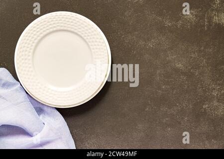 Draufsicht auf leeren geservierten Teller, graue Textilserviette auf schwarzem Beton-Hintergrund. Speicherplatz kopieren. Stockfoto
