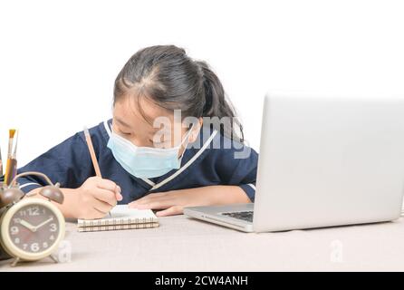 Asiatische Schüler tragen Schutzmaske, Notizen von Laptop-Computer isoliert auf weißem Hintergrund, schreiben Hausaufgaben, neue normale und COVID verhindern Stockfoto