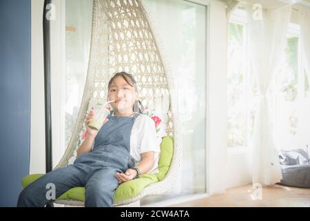 Nettes Mädchen trägt eine Denim Overalls trinkt Eis grünen Tee und entspannen Sie sich im weißen Haus. Freizeit und Relax-Konzept Stockfoto