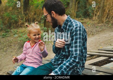 Baby und Vater spielen im Herbstpark. Vater und Tochter sitzen draußen auf einer Holzbrücke. Glückliche Familienmomente der Kindheit. Stockfoto