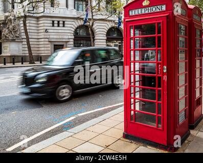 Ikonisches London - ein London Taxi fährt an zwei traditionellen roten Telefonzellen im Zentrum von London vorbei. Bewegungsunschärfe der Taxibewegung. London Tourism. Stockfoto