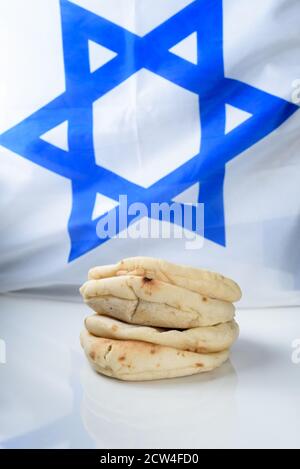 Stapeln Sie frisch gebackene Pittas auf Holzbrett über israel Flagge Hintergrund. Frisch aufgebautes Pita-Brot auf weißem Tisch. Stockfoto