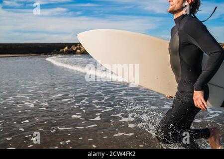 Porträt eines jungen Surfers, der das Wasser verlässt, mit Surfbrett unter seinem Arm. Sport und Wassersport Konzept. Stockfoto