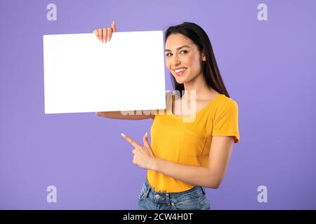 Glückliche junge Dame zeigt auf weiße Papiertafel Stockfoto