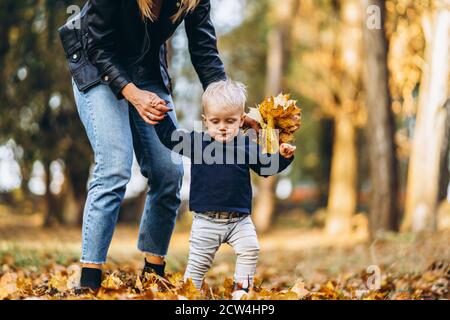 Glückliche Mutter mit ihrem kleinen Sohn haben Spaß im Stadtpark mit bunten Blättern im Herbst. Glückliche Familie, Muttertagskonzept Stockfoto