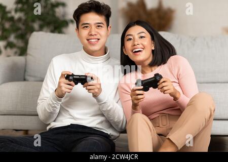 Chinesisches Paar Spielen Video Spiel Sitzen Auf Sofa Innen Stockfoto