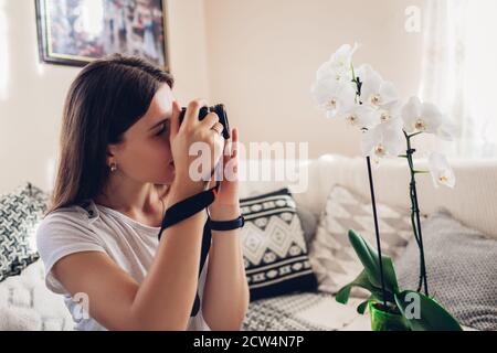 Fotografin fotografiert die blühende Orchidee mit der Kamera. Freiberufler arbeitet von zu Hause aus während covid Stockfoto