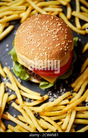 Cheeseburger umgeben von pommes auf einem schwarzen Tisch Stockfoto