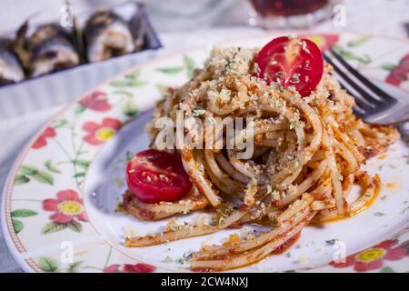 Sizilianisches Rezept: Spaghetti 'c'anciova e muddica atturrata' (mit Sardellen und gerösteten Paniermehl) und Sardinen im Hintergrund Stockfoto