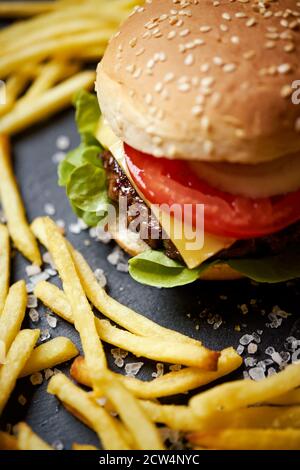 Cheeseburger umgeben von pommes auf einem schwarzen Tisch Stockfoto