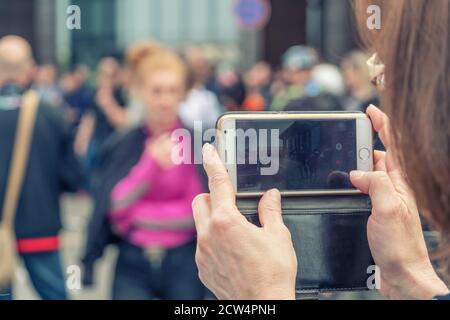 Bild von weiblichen Händen halten ein Handy, das schießt Eine Show auf der Straße Stockfoto