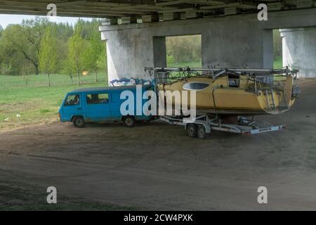 Blauer LKW trägt ein gelbes Boot. Foto LKW auf der Straße unter der Brücke. Stockfoto