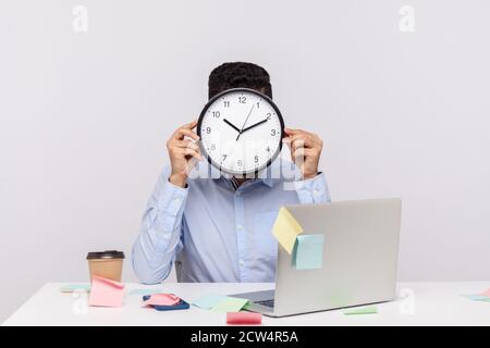 Überstunden. Anonymer Mann Mitarbeiter sitzt im Büro Arbeitsplatz, versteckt Gesicht hinter der Uhr, klebrige Notizen rund um erinnern an Termin, stressig Stockfoto