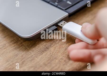 Nahaufnahme der Hand der Frau, die USB-Flash-Laufwerk in den Laptop einsteckt Auf einem Holztisch Stockfoto