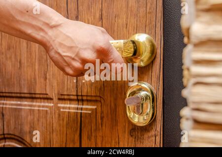 Männliche Hand, die einen goldenen Griff aus braunem Holz hält Nahaufnahme der Tür Stockfoto