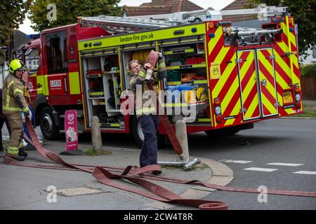 Die Feuerwehrfrau rollt den Schlauch mit der Londoner Feuerwehr aus, die an einem Hausbrand in einer Wohnstraße in South London, England, Großbritannien teilnimmt Stockfoto